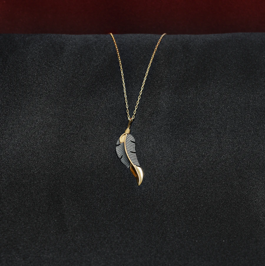 Gold feather pendant on a fine chain, on black velvet