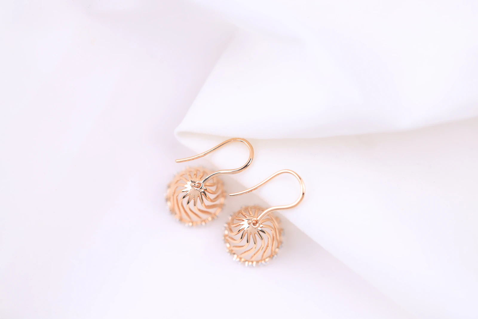 Rose gold drop earrings resting on white silk